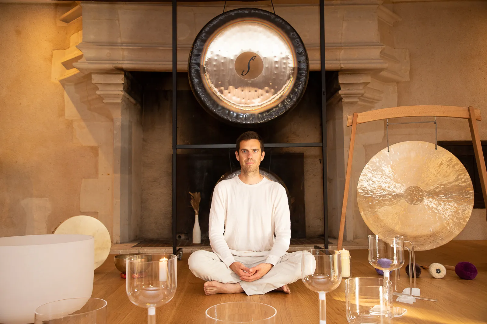 Alexandre Tonnelier assis en tailleur au milieu de bols de cristal et de gongs, dans une salle aux murs de pierre